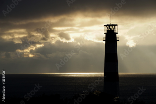 Lighthouse on the sea under stormy clouds at sunset