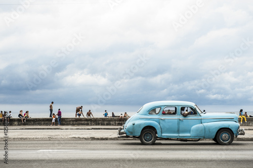 Photography HAVANA, CUBA - MAY 18, 2011: Classic vintage American car serving as taxi drives along the seafront Malecon, a popular place for socializing in Central Havana