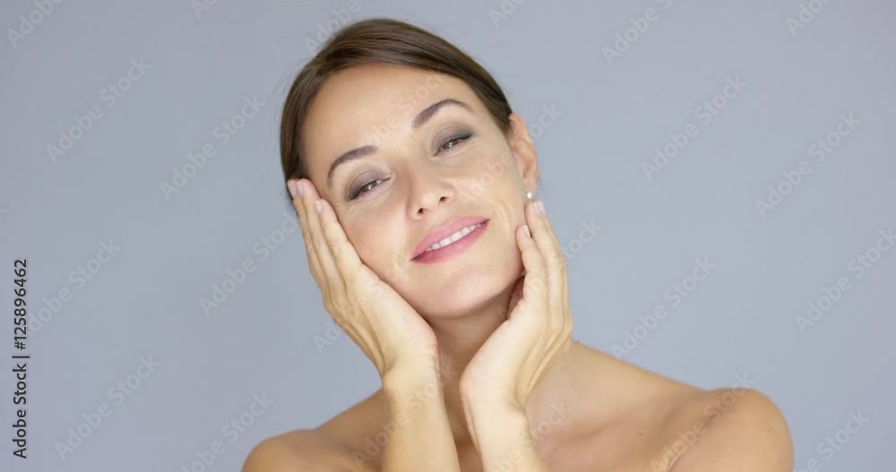 Grinning young adult female with head resting on hands over gray background with copy space Grinning young adult female with head resting on hands over gray background with copy space