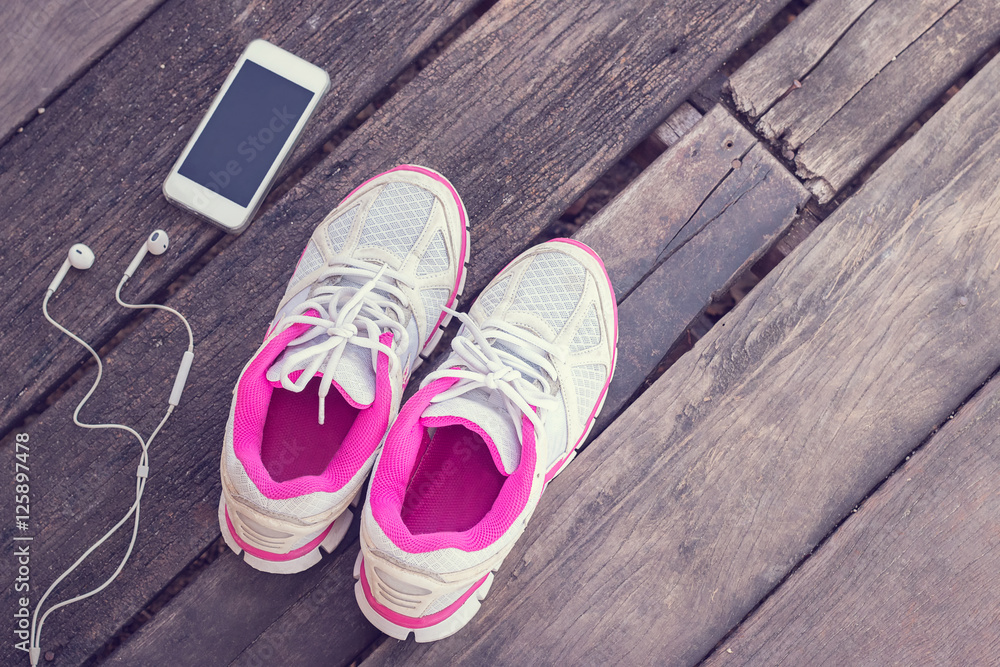 Running shoes and phone with headphones on old wooden background