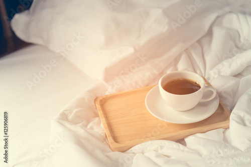 Cup of coffee with wooden tray on bed background