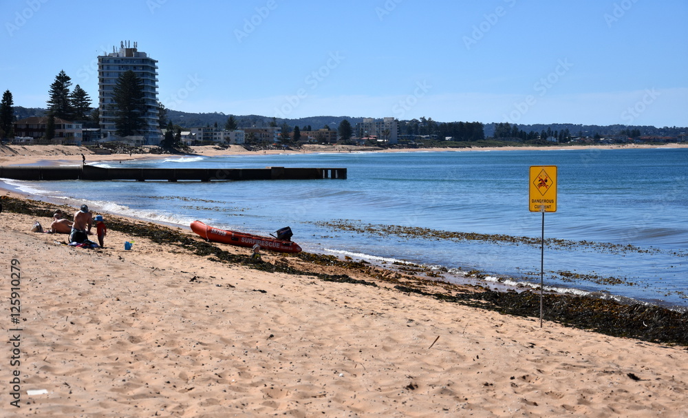 Sydney, Australia - Nov 5, 2016. A sign reads Dangerous Current. Seaweeds on the sand.