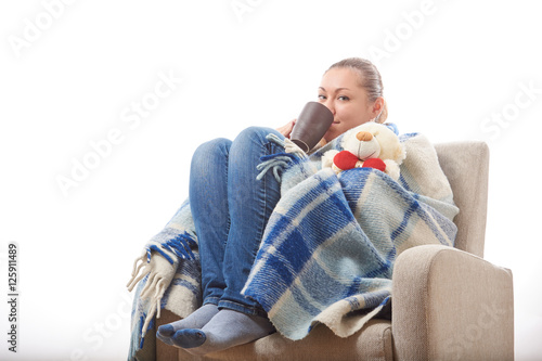 Beautiful girl resting and drinking tea sitting wrapped in a woolen plaid blanket.
