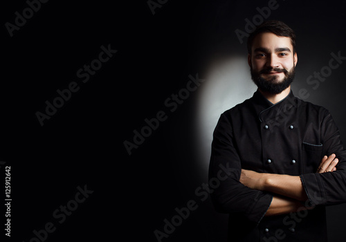 Professional chef with a beard in black uniform on a black background