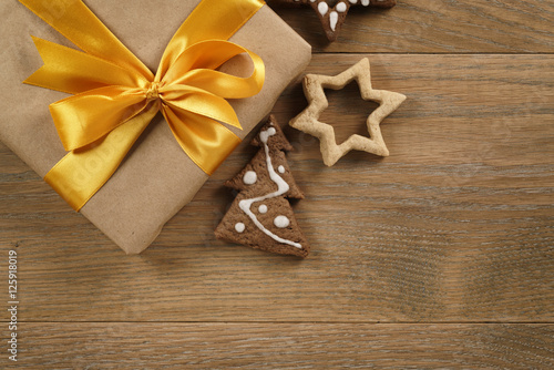 gift box with golden ribbon bow and christmas cookies on wood table