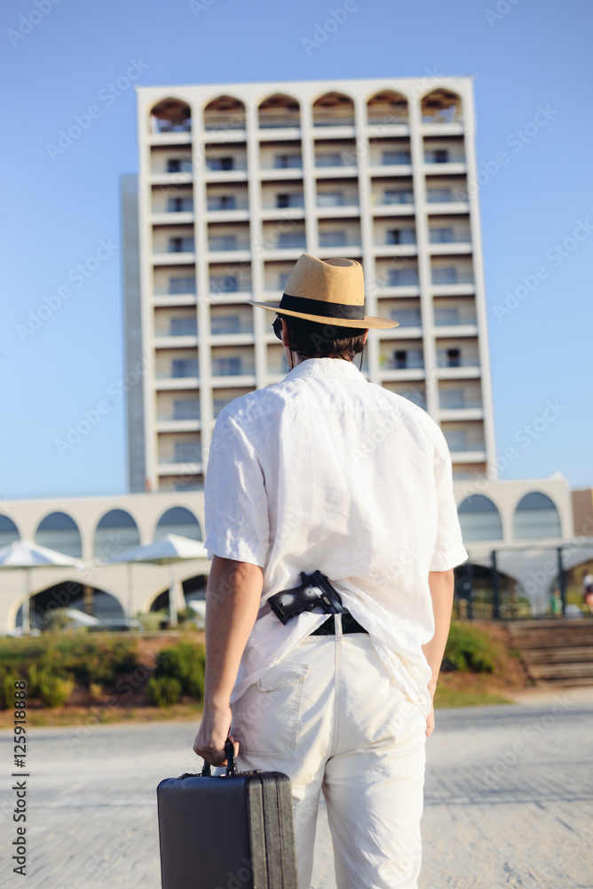 Rear view of man holding gun and briefcase on sunny outdoors background Rear view of man holding gun and briefcase on sunny outdoors background