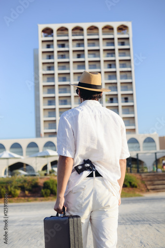 Rear view of man holding gun and briefcase on sunny outdoors background