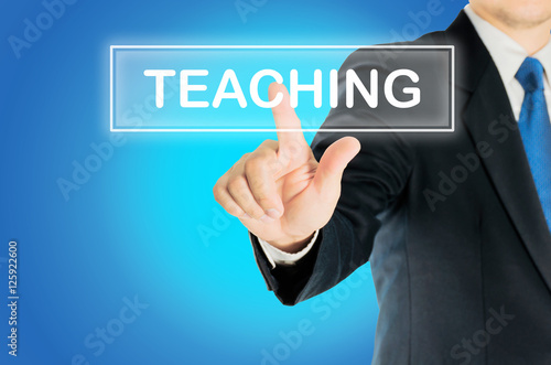Business man is pushing TEACHING transparent button word over blue gradient background, business concept