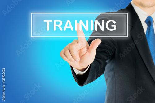 Business man is pushing TRAINING transparent button word over blue gradient background, business concept