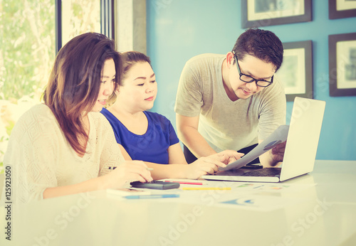 Vintage style photo of two women and one man are working with at computer in modern office