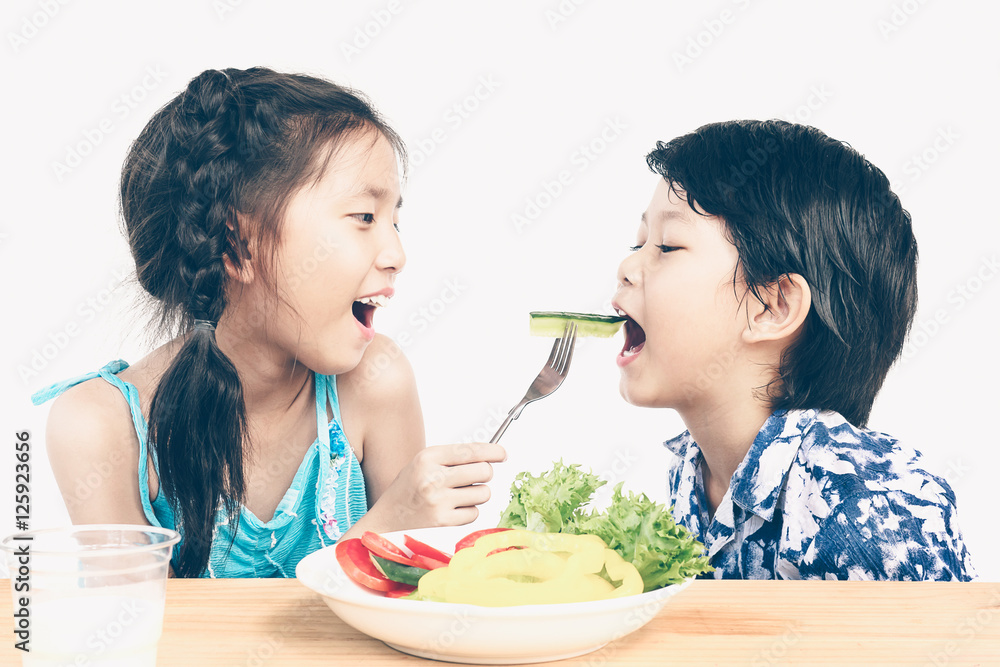 Asian boy and girl are happily eating fresh vegetable salad with Asian boy and girl are happily eating fresh vegetable salad with