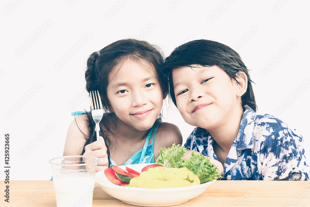 Asian boy and girl are happily eating fresh vegetable salad with Asian boy and girl are happily eating fresh vegetable salad with
