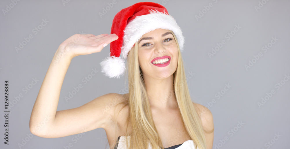 Pretty young girl doing hello hand gesture. She wearing Santa Claus red hat. Smiling and looking to the camera. Pretty young girl doing hello hand gesture. She wearing Santa Claus red hat. Smiling and looking to the camera.
