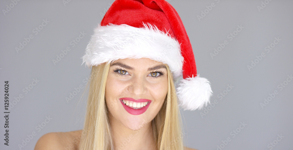 Beautiful chick in Santa Claus Hat posing with sensual smile while isolated on gray background. She has long blond hair and bare shoulders. Beautiful chick in Santa Claus Hat posing with sensual smile while isolated on gray background. She has long blond hair and bare shoulders.