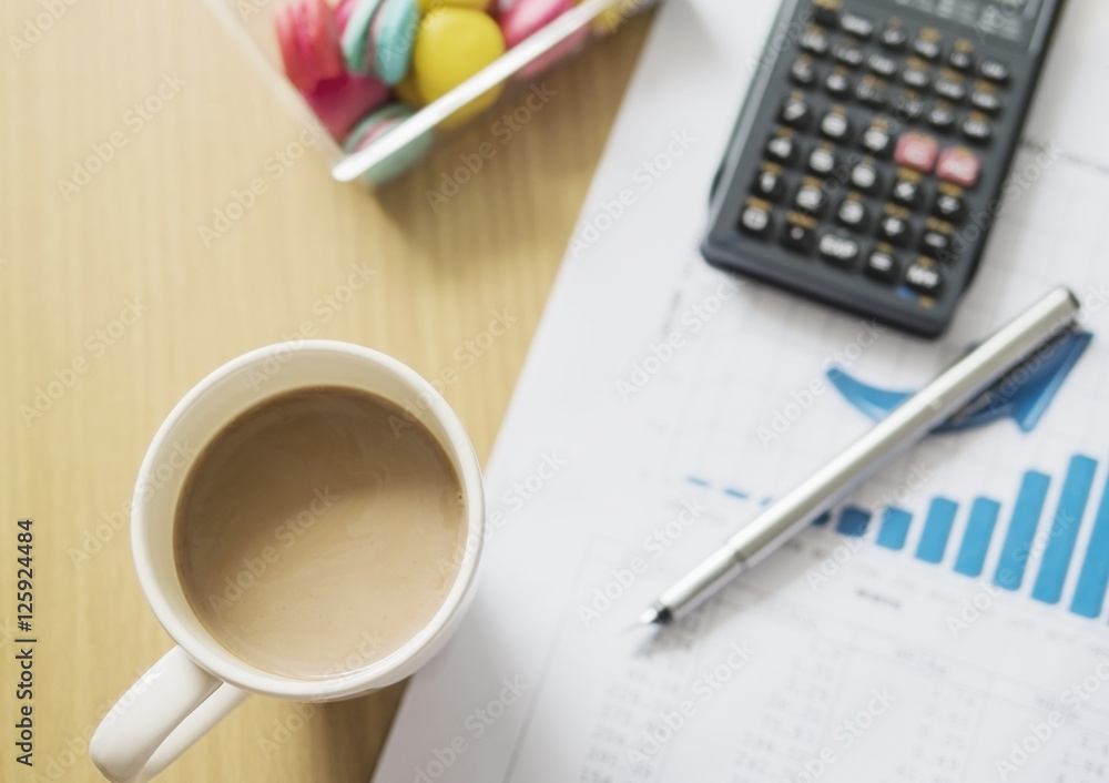 Business financial working concept, pen an calculator on growth bar graph with coffee cup and macaroon background selective focused Business financial working concept, pen an calculator on growth bar graph with coffee cup and macaroon background selective focused