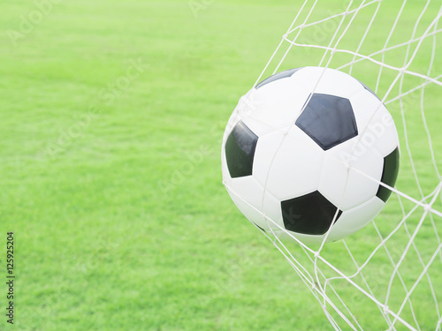 Shooting shot, football in goal net with green grass field background © pairhandmade