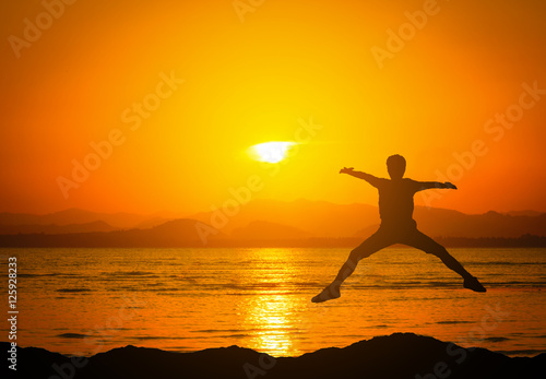 Silhouette of jumping man on mountains near the beach at sunset.