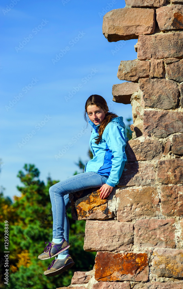 Teenage girl sitting on ruined wall of old castle Teenage girl sitting on ruined wall of old castle