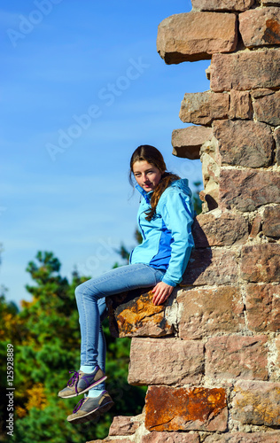 Teenage girl sitting on ruined wall of old castle