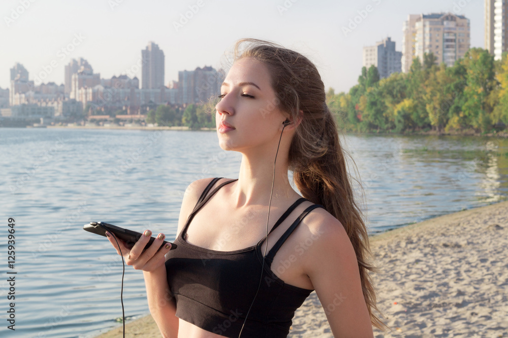 Young girl at coast listening to music on cell phone