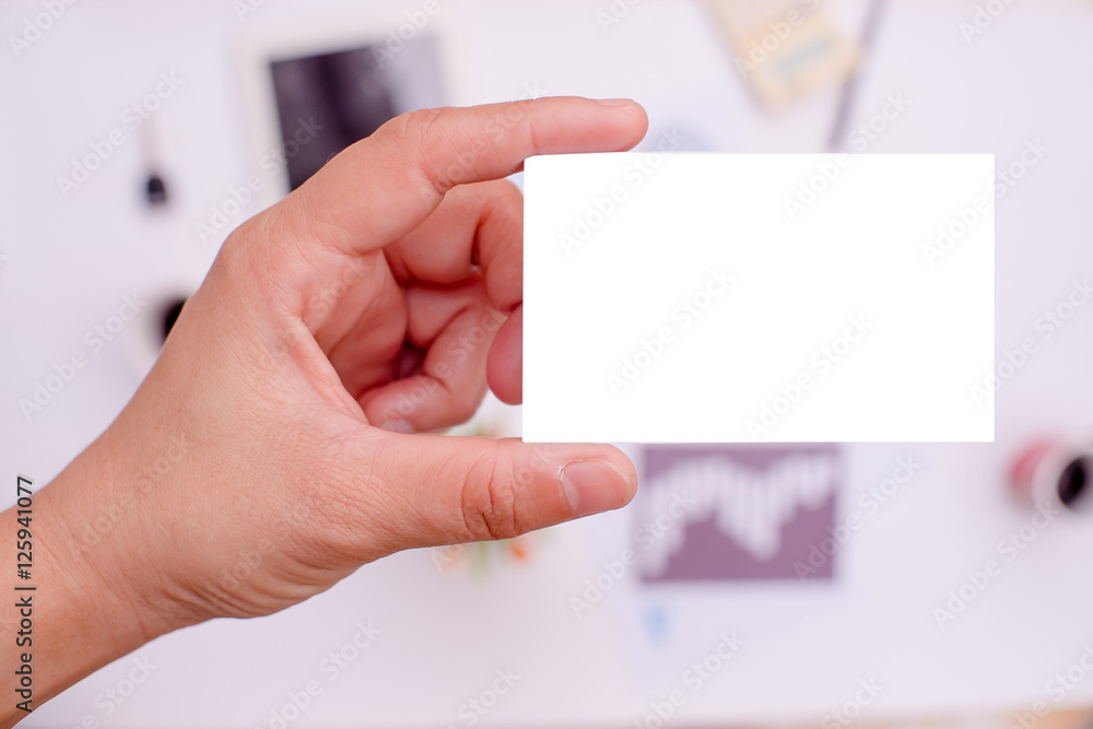 Hand is holding a white business card or white label On the desk in office. Hand is holding a white business card or white label On the desk in office.