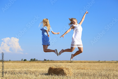 Two beautiful young women jumping in wheat field