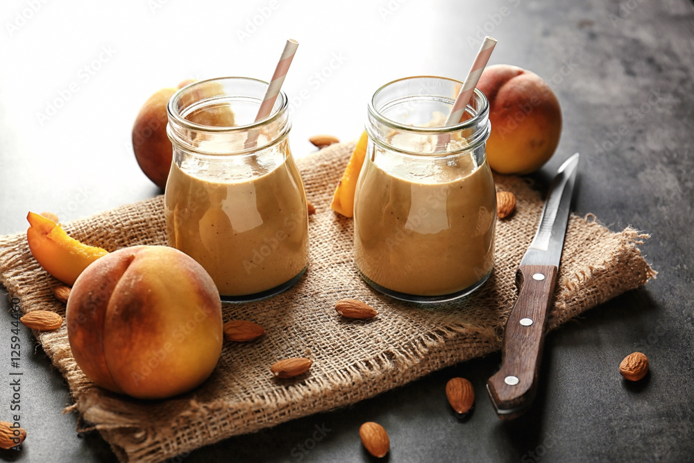 Fototapeta premium Mason jars with smoothie, peaches and napkin on grey table