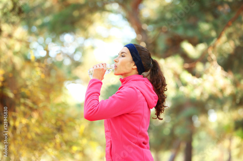 Sporty young woman drinking water in autumn park