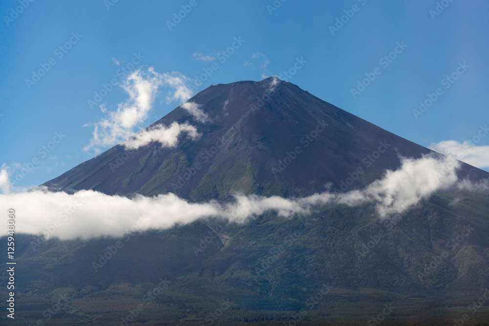Hakone, Japan - September 27, 2016: The summit of mount Fuji against blue sky clearly visible from the Fujikya area. A few white clouds create a band halfway up the mountain. Forested foreground.