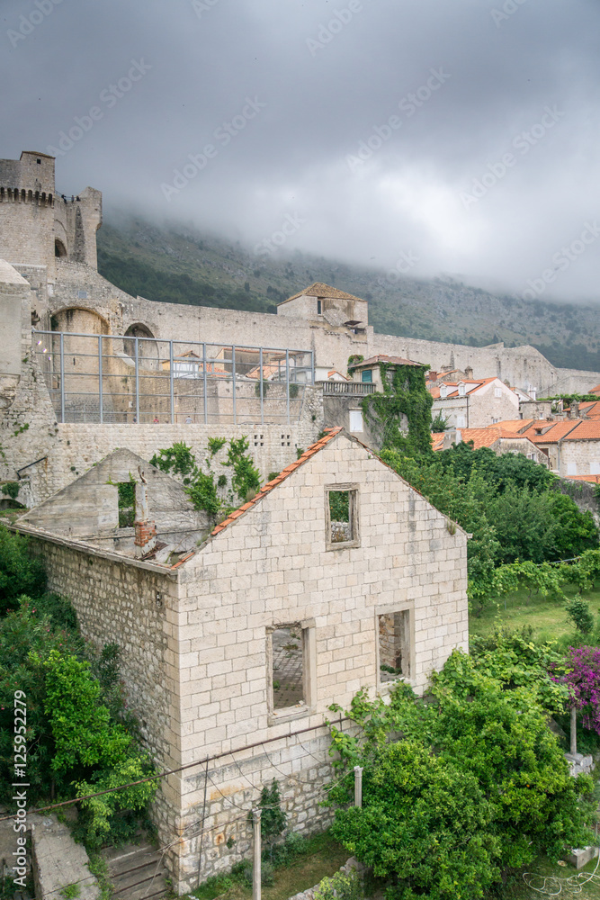 Ominous storm clouds cover Mount Srd, which sits behind the old town of Dubrovnik, Croatia, with war damaged buildings visible in the foreground, and the city walls and fortifications visible in the b