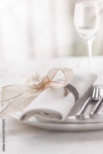 Beautifully elegant decorated table for holiday - wedding or valentine day with modern cutlery, bow, glass, candle and gift, closeup, toned