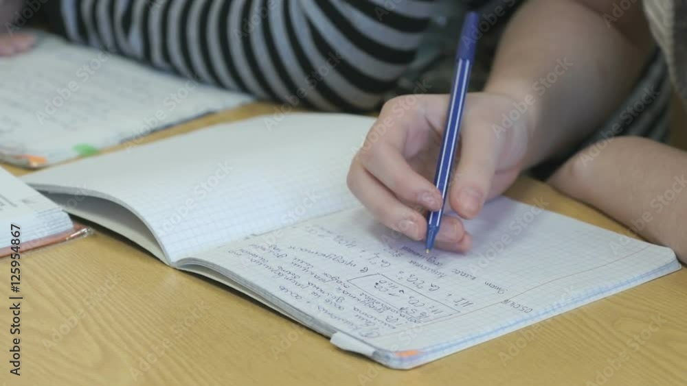 Pupil writes text in a exercise book using a pen Pupil writes text in a exercise book using a pen