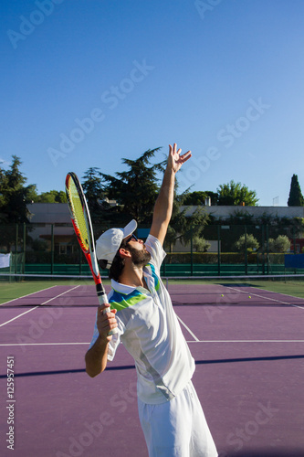 Professional tennis player is doing a kick tennis on a tennis court on a sunny summer morning. He is dressed in sportswear. 