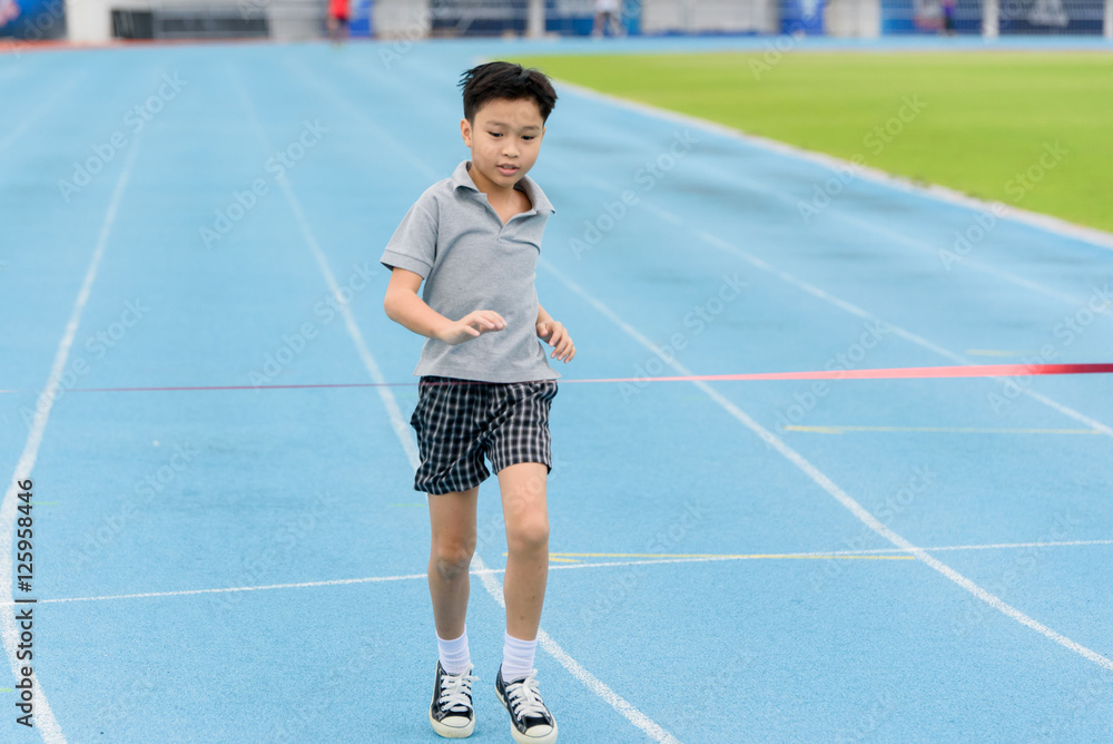 Obraz premium Young Asian boy running on blue track in the stadium