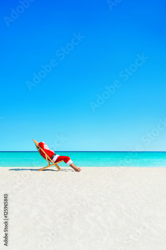 Christmas Santa Claus relaxing in sunlounger at ocean tropical beach