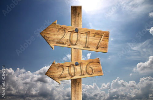 Wood sign of 2016 and 2017 in in left on blue sky background.