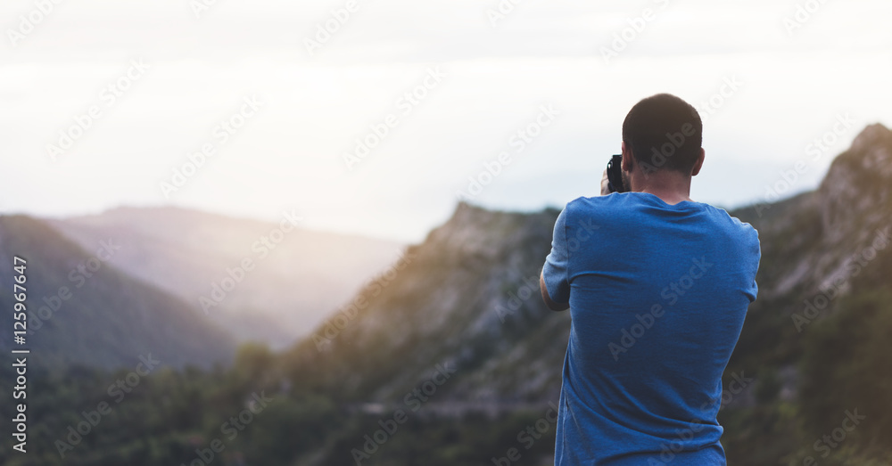 Hipster man enjoying sunset on peak of foggy mountain, tourist traveler taking pictures of amazing landscape on digital camera on background valley view mockup, photographer looking nature sunrise