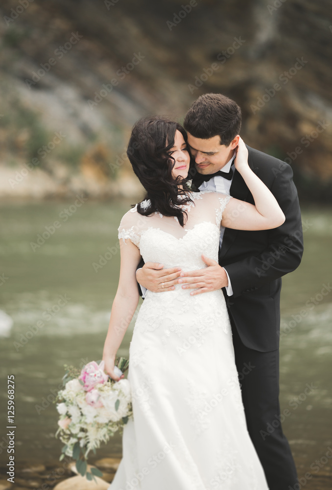 Elegant gentle stylish groom and bride near river with stones. Wedding couple in love Elegant gentle stylish groom and bride near river with stones. Wedding couple in love