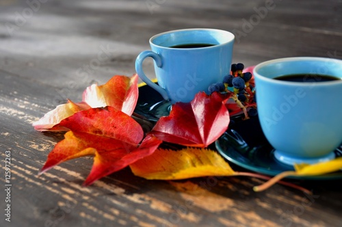 two blue cups of coffee on rustic wooden table decorated with colorful leaves