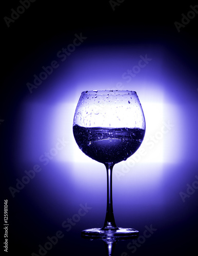 Pouring water into wine glass with black background blue white balnce photo