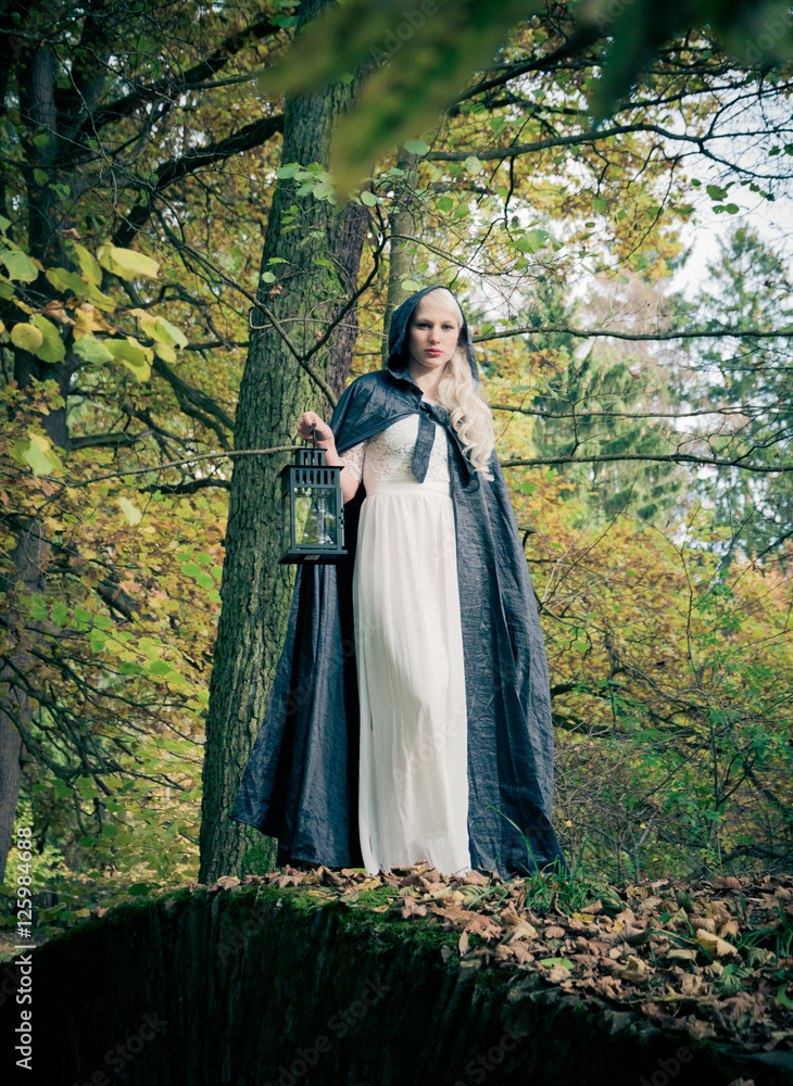 Woman with black coat and a lantern in a forest Woman with black coat and a lantern in a forest