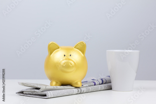 gold piggy bank on newspaper with coffee cup