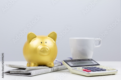 gold piggy bank on newspaper with coffee cup and calculator