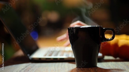 Footage of a person typing on a computer and grabbing a steamy coffee mug.