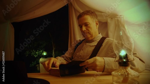 An old west eighteenth century type man in a tent reads from his Bible.