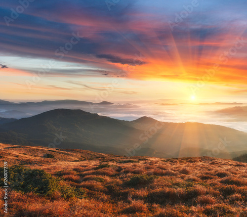 Beautiful landscape in the autumn mountains at sunset. Dramatic colorful sky. View of foggy hills covered by forest. 