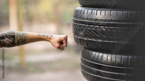 Woman boxer with tatto arms at workout. Young woman is boxing punching bag from car tires. At the head of the girl dreadlocks. Toned photo.