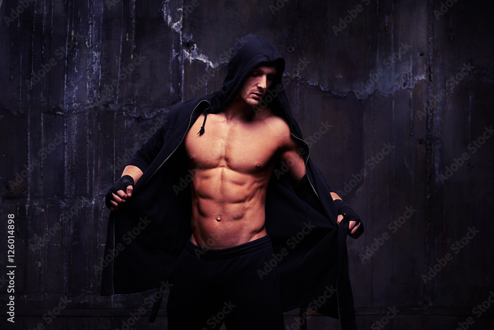 Bare-chested muscular athlete taking off a black hoodie