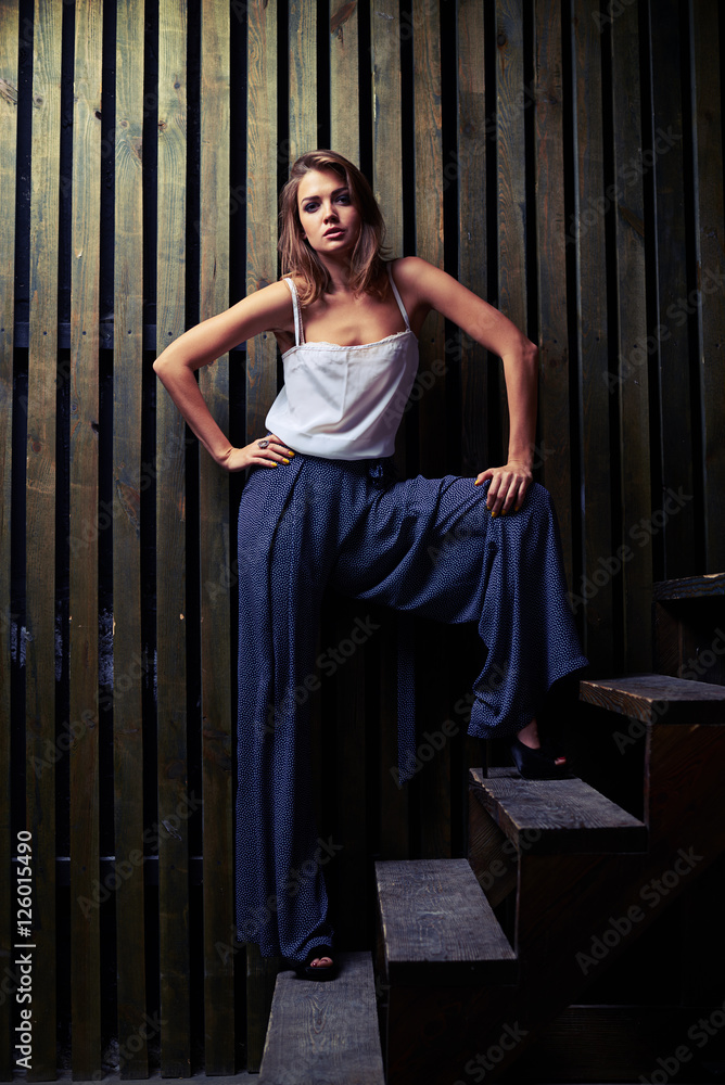 Modern fashion model posing in wide stance on wooden stairs, flo Modern fashion model posing in wide stance on wooden stairs, flo