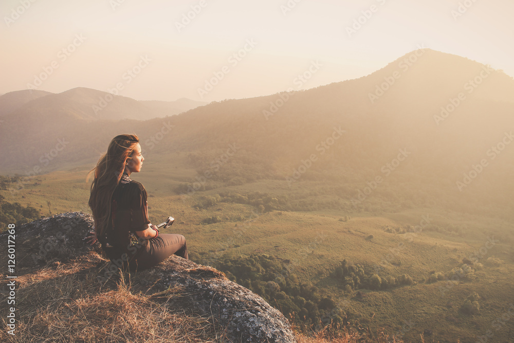 Hipster young girl with backpack enjoying sunset on peak of foggy mountain. Tourist traveler on background view mockup. Hiker looking sunlight in trip in Thailand country. Vintage filtered image. Hipster young girl with backpack enjoying sunset on peak of foggy mountain. Tourist traveler on background view mockup. Hiker looking sunlight in trip in Thailand country. Vintage filtered image.